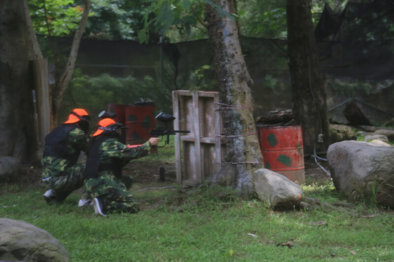 看看兩名橘隊成員躲在遮蔽物後方，在激烈的槍林彈雨中抓住機會拼命射擊